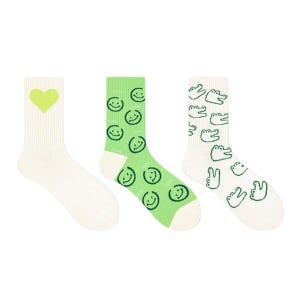Könnte beinhalten: Drei Paar Crew-Socken. Ein Paar ist weiß mit einem limettengrünen Herz, ein anderes ist grün mit Smiley-Gesichtern, und das letzte ist weiß mit grünen Alligatoren und Peace-Zeichen-Grafiken.