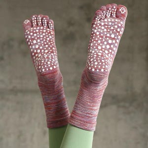 Op de afbeelding: Rode en paarse teensokken met witte stippen op de zolen. De sokken worden gedragen met groene leggings. De voeten zijn omhoog.