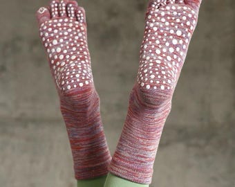 May include: A pair of red and purple toe socks with white polka dots on the soles. The socks are worn with green leggings, and the feet are raised in the air.