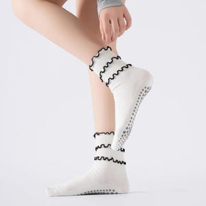 May include: White socks with a ruffled black trim. The socks have a non-slip grip on the soles. The socks are ribbed and are mid-calf length.