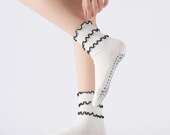 May include: White socks with a ruffled black trim. The socks have a non-slip grip on the soles. The socks are ribbed and are mid-calf length.
