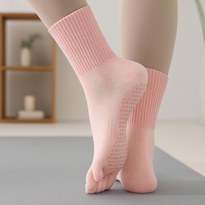 May include: Pale pink socks with ribbed cuffs and a dotted pattern on the soles. These socks are designed for comfort and grip, suitable for yoga or Pilates. The socks are shown on a person's feet.