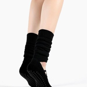 May include: Black yoga socks with non-slip grips on the soles. The socks are designed to cover the foot and ankle, with a ribbed knit upper that extends up the calf. The socks are shown on a white background.