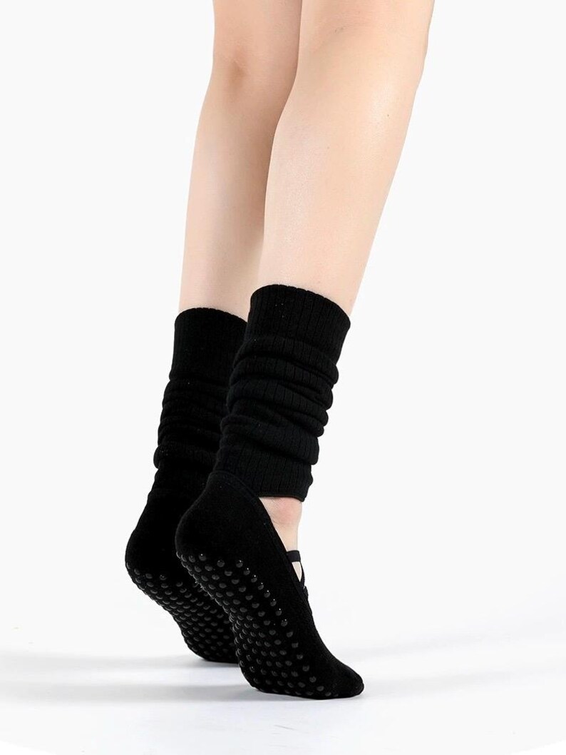 May include: Black yoga socks with non-slip grips on the soles. The socks are designed to cover the foot and ankle, with a ribbed knit upper that extends up the calf. The socks are shown on a white background.