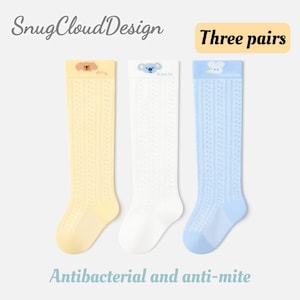 May include: Three pairs of knee-high socks in yellow, white, and blue. Each pair features a different animal design: a dog, a koala, and a bunny. The socks have a delicate, openwork pattern and the text "Antibacterial and anti-mite".