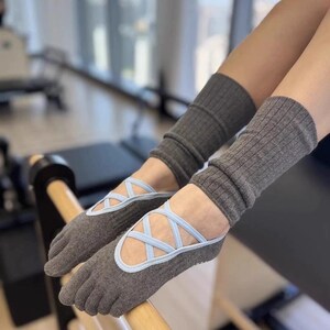 May include: Gray toe socks with light blue crisscross straps, resembling ballet flats, paired with matching gray leg warmers. The socks have a ribbed texture and are designed for comfort and support during exercise or dance activities.