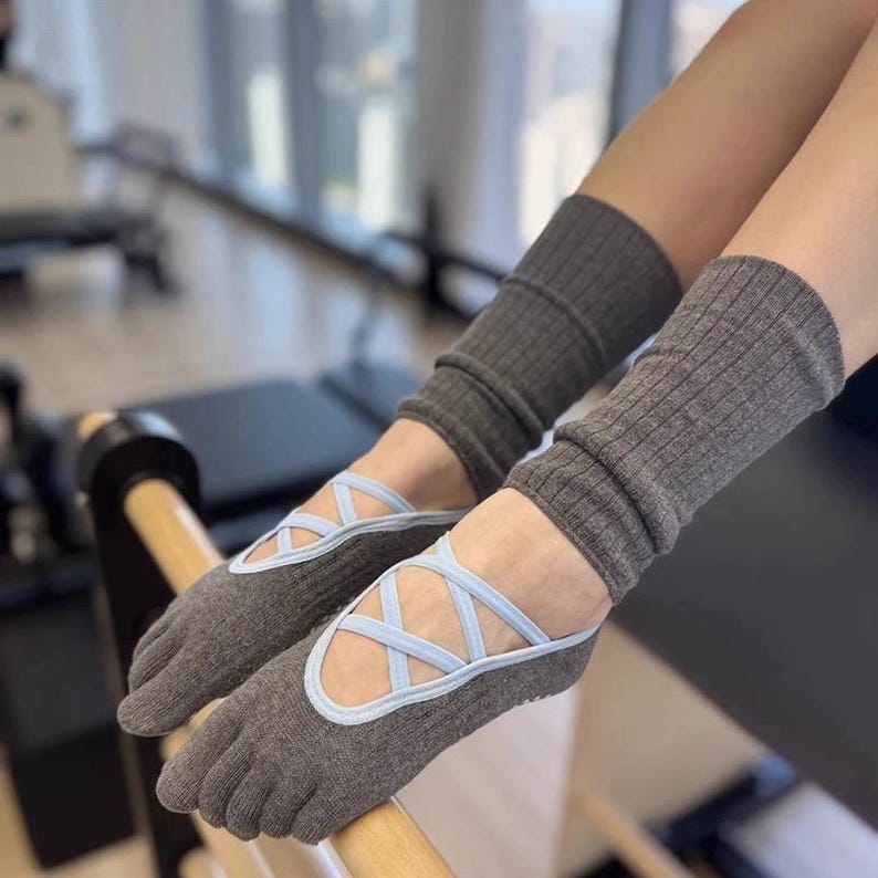 May include: Gray toe socks with light blue crisscross straps, resembling ballet flats, paired with matching gray leg warmers. The socks have a ribbed texture and are designed for comfort and support during exercise or dance activities.