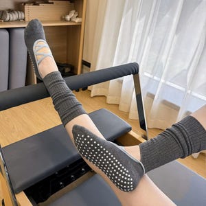 May include: Gray Pilates socks with a crisscross design and non-slip soles. The socks are paired with matching gray leg warmers. The socks and leg warmers are designed for exercise and fitness activities.