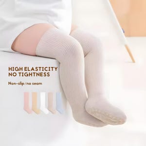 May include: White ribbed knee-high tights for babies and toddlers. The tights are seamless and have a non-slip grip on the soles. The text "HIGH ELASTICITY NO TIGHTNESS" and "Non-slip/no seam" is printed on the image.  Five pairs of tights in different colors are shown below the main image.