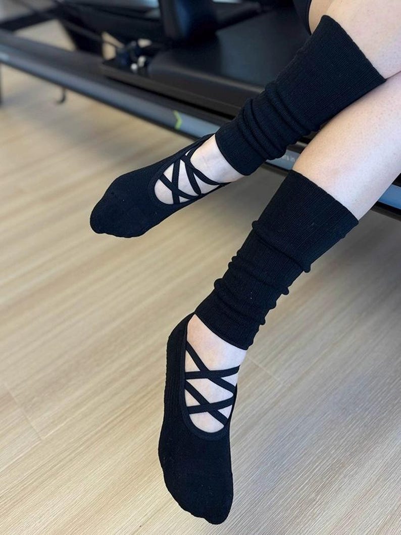 May include: Black ballet-style socks with crisscross straps and ribbed leg warmers. The socks have a flat sole and are designed to be worn during exercise or dance. The leg warmers are long and provide extra warmth and support.