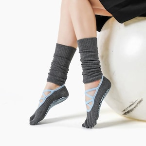 Puede incluir: Calcetines de yoga grises con correas azules y un diseño de punta dividida. Los calcetines tienen un agarre antideslizante en las suelas y se combinan con calentadores de piernas grises. Diseñados para yoga y Pilates.