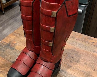 May include: A pair of red leather boots with black accents and buckles. The boots have a rugged, textured sole.