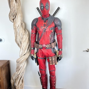 Pode incluir: Um traje de corpo inteiro do Deadpool com um fato texturizado vermelho e preto, uma máscara completa a condizer com lentes oculares brancas, um cinto utilitário com fivela de logótipo circular, ombreiras, coldres de perna e duas katanas.