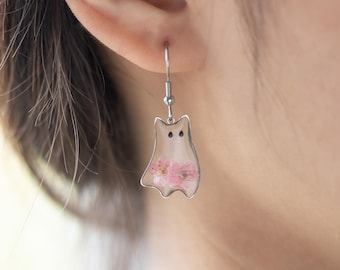 May include: Silver dangle earrings with a clear resin ghost shape filled with pink pressed flowers.