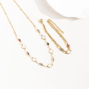 May include: A gold necklace and bracelet set with white clover charms and colorful gemstones. The necklace and bracelet are both delicate and feminine.