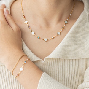 May include: A gold necklace and bracelet set with white clover charms and colorful crystal accents. The necklace features a delicate chain with small white beads and the bracelet has a simple chain with a single clover charm.