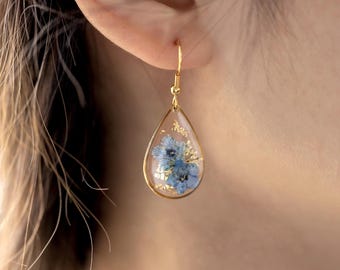 May include: Gold teardrop earrings with a clear resin setting containing pressed blue flowers.