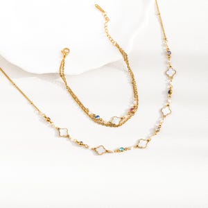 May include: A gold necklace and bracelet set with white clover charms and colorful gemstones. The necklace has a delicate chain and the bracelet is a double chain.