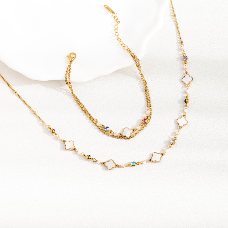 May include: A gold necklace and bracelet set with white clover charms and colorful gemstones. The necklace has a delicate chain and the bracelet is a double chain.