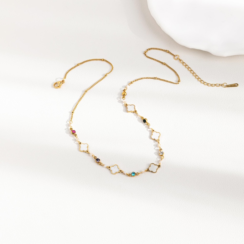 May include: A gold necklace with a delicate chain and white clover charms accented with colorful gemstones.
