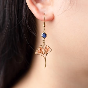 May include: Gold earrings with a blue gemstone and a clear resin ginkgo leaf with pressed orange flowers.