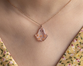 May include: A rose gold chain necklace with a pink ghost charm. The ghost is decorated with small yellow flowers.