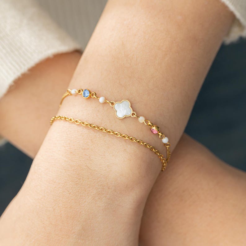May include: A gold chain bracelet with a white clover charm and colorful crystals.