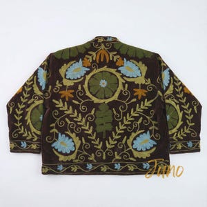 May include: A brown jacket with intricate floral embroidery in shades of green, blue, and orange. The jacket features a round collar and long sleeves. The embroidery is detailed with leaves and flowers, creating a decorative pattern.