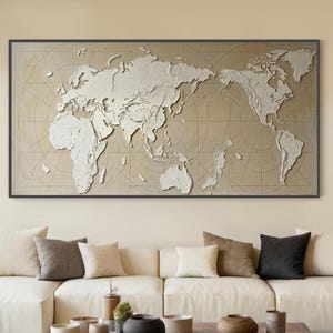 Può includere: Una grande opera d'arte con mappa del mondo incorniciata con continenti in rilievo bianco su sfondo beige. L'opera è appesa sopra un divano bianco con cuscini. Un tavolino da caffè in legno scuro e oggetti decorativi completano il soggiorno.