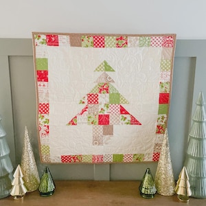 May include: A quilted Christmas tree wall hanging. The tree is made of red, green, and tan patterned squares on a white background. The quilt is framed with a border of matching fabrics. Decorative Christmas trees in various sizes and colors are displayed below.
