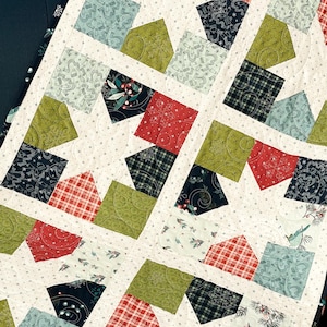May include: A handmade quilt featuring a patchwork design with various fabric patterns. The quilt showcases squares and triangles in shades of red, green, blue, and black, set against a white background with small, scattered dots. The quilt is a cozy, decorative textile.