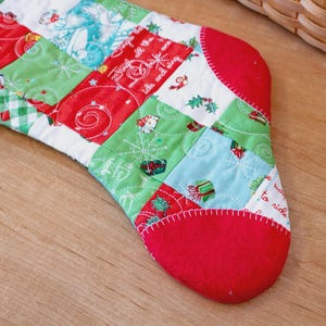 May include: A festive Christmas stocking with a patchwork design. It features red, green, and white squares with seasonal patterns. The toe and cuff are a solid red colour. The stocking is handmade.
