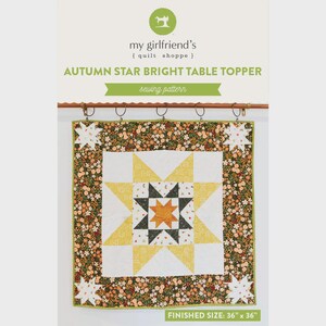 Peut inclure: Une courtepointe carrée avec un motif d'étoile, avec des couleurs jaune, blanc, noir et orange. La courtepointe a une bordure florale et des accents d'étoiles. Le texte "AUTUMN STAR BRIGHT TABLE TOPPER" et "sewing pattern" sont visibles. Taille finie : 91 cm x 91 cm.