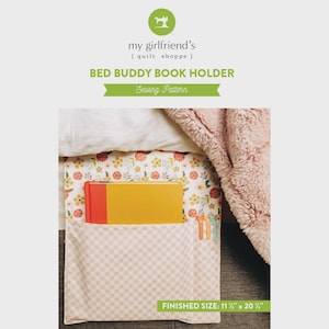 May include: A sewing pattern for a Bed Buddy Book Holder by my girlfriend's quilt shoppe. The pattern features a fabric organizer with a floral print and a beige gingham pocket, holding a yellow book. Finished size is 11.5 inches by 20.5 inches.