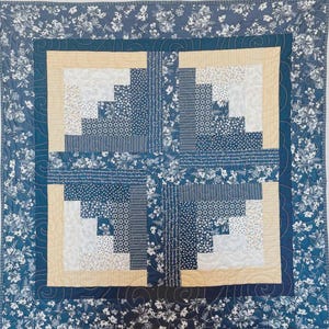 Peut inclure: Une courtepointe faite à la main avec un motif central de quatre blocs de cabane en rondins dans des tons de bleu, crème et blanc. Les blocs sont entourés d'une bordure crème et d'une bordure bleue à motifs floraux. Un élément de décoration intérieure.