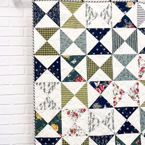 Könnte beinhalten: Ein Patchwork-Quilt mit einem sich wiederholenden Fliegen-Muster. Das Design umfasst verschiedene Stoffdrucke in Marineblau, Olivgrün und Weiß, akzentuiert durch florale Motive, Vichy-Karos und Streifenmuster mit einer sichtbaren Steppung.