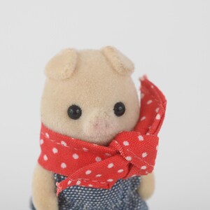 Puede incluir: Figura de cerdo beige claro con ojos negros y hocico rosa. Lleva un pa&ntilde;uelo rojo con lunares blancos y un atuendo de estilo denim azul. El juguete tiene orejas peque&ntilde;as y redondeadas.