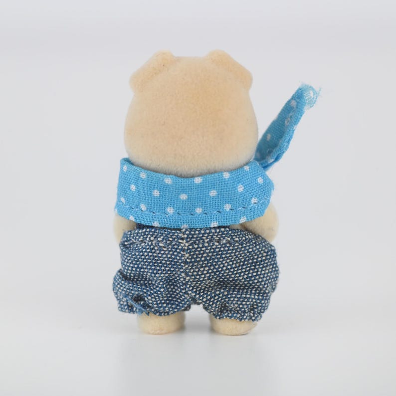 Puede incluir: Peque&ntilde;a figura de animal de color beige, con un pa&ntilde;uelo azul con lunares blancos y pantalones cortos vaqueros. La figura se ve desde atr&aacute;s, mostrando los detalles de la ropa y las orejas del animal.