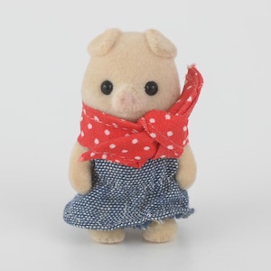 Puede incluir: Peque&ntilde;a figura de cerdo beige, con un pa&ntilde;uelo rojo de lunares blancos y un vestido vaquero azul. El cerdo tiene ojos negros y un hocico rosa. La figura est&aacute; de pie sobre un fondo blanco.
