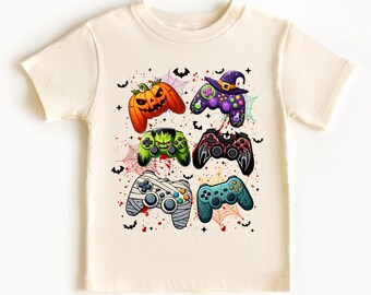 Op de afbeelding: Crèmekleurig T-shirt met zes kleurrijke Halloween-thema gamecontroller-ontwerpen. De controllers bevatten een pompoen, een heks, een Frankenstein-monster en anderen. Vleermuizen, spinnenwebben en rode spatten maken het spookachtige ontwerp compleet.