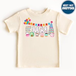 Puede incluir: Una camiseta de color crema con una pancarta de cumpleaños colorida y el nombre "EMMA" escrito en letras grandes. Cada letra está decorada con un patrón colorido diferente y un lindo personaje de dibujos animados.