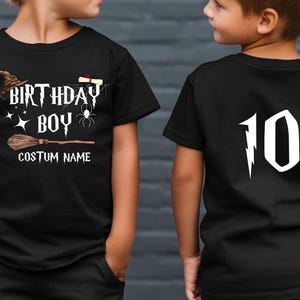 Op de afbeelding: Zwart T-shirt met een verjaardagsthema. De voorkant heeft de woorden "BIRTHDAY BOY" met een heksenhoed, bezem en spinnenafbeelding. De achterkant toont het nummer "10" in wit met een bliksemontwerp.