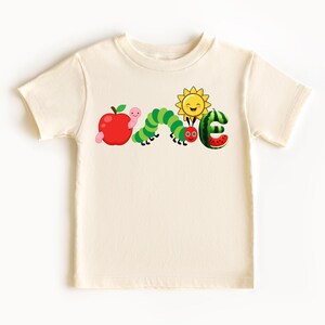 a white t - shirt with a picture of a caterpillar and an apple