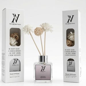 May include: A clear glass reed diffuser with a silver collar and a light pink label, featuring the text "The Aroma Vault." The diffuser is accompanied by white flowers and a woven ball. The packaging includes the text "In every scent, a hidden memory, in every aroma, a new discovery."