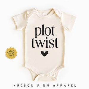 May include: Cream-colored baby bodysuit with the words "plot twist" in black, a black heart graphic, and the text "HUDSON FINN APPAREL" at the bottom. A yellow sticker with the words "ships next day" is on the left.
