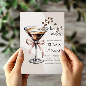 May include: A birthday invitation card featuring a watercolor illustration of a martini with coffee beans. The text reads "a tini bit older" and invites guests to celebrate Ella's 25th birthday. The card is held by a person.