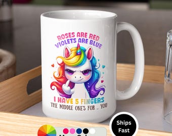 May include: White ceramic coffee mug with a colorful illustration of a unicorn with a middle finger up. The text reads "Roses are red, Violets are blue, I have 5 fingers, the middle one's for you."