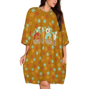 May include: A mustard yellow t-shirt dress featuring a repeating pattern of small red, orange, and light blue flowers. The center of the dress displays the word GIGI in large, stylized letters with a leopard print fill and floral accents.