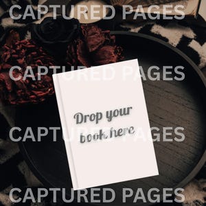 May include: A white book with the text "Drop your book here" is on a dark wooden tray. The tray is surrounded by black roses and dried red flowers. The background includes an open book and a black and white patterned blanket.