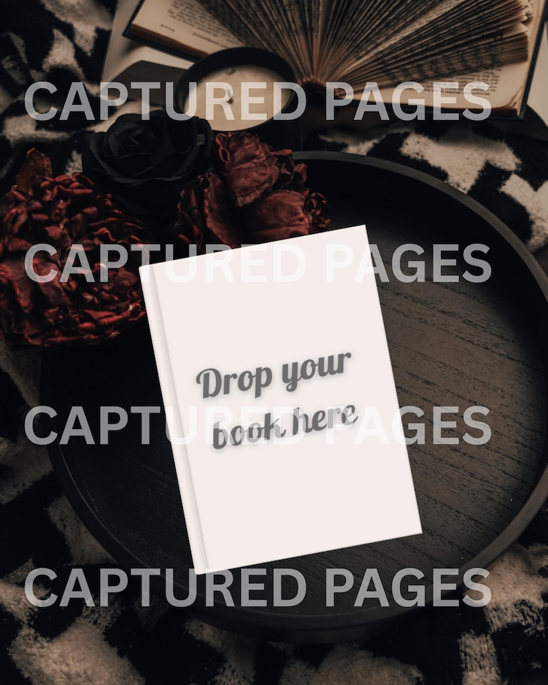 May include: A white book with the text "Drop your book here" is on a dark wooden tray. The tray is surrounded by black roses and dried red flowers. The background includes an open book and a black and white patterned blanket.